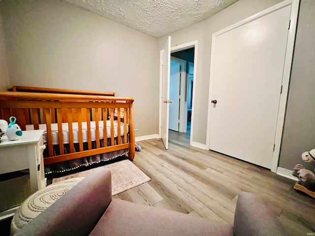 bedroom featuring light wood-type flooring, a textured ceiling, and a nursery area