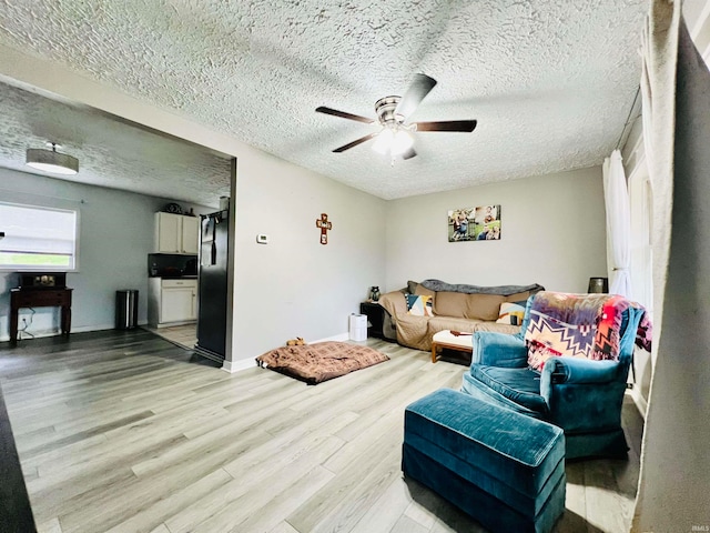 living room with ceiling fan, light wood-type flooring, and a textured ceiling