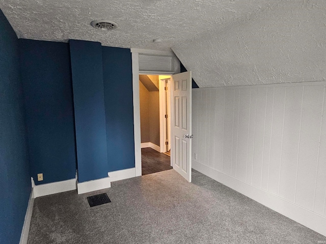 additional living space featuring a textured ceiling, dark carpet, and vaulted ceiling