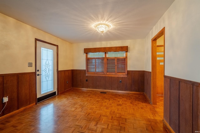 entryway with wooden walls, light parquet flooring, and a chandelier