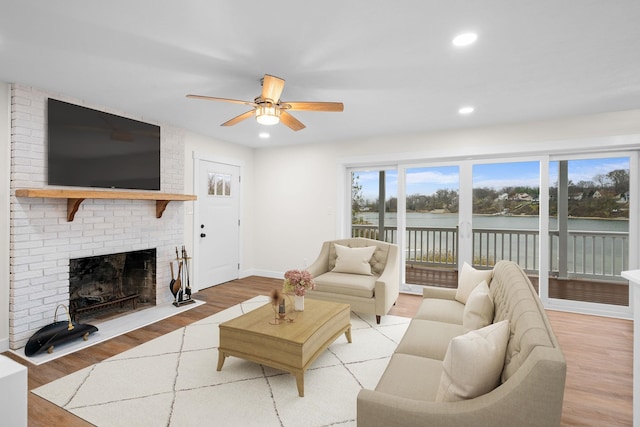 living room featuring a fireplace, light wood-type flooring, a water view, and ceiling fan