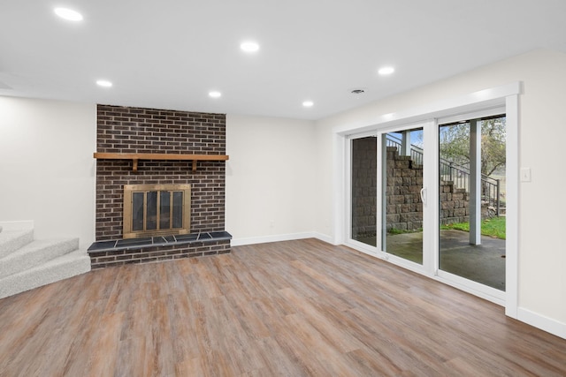 unfurnished living room featuring wood-type flooring and a brick fireplace