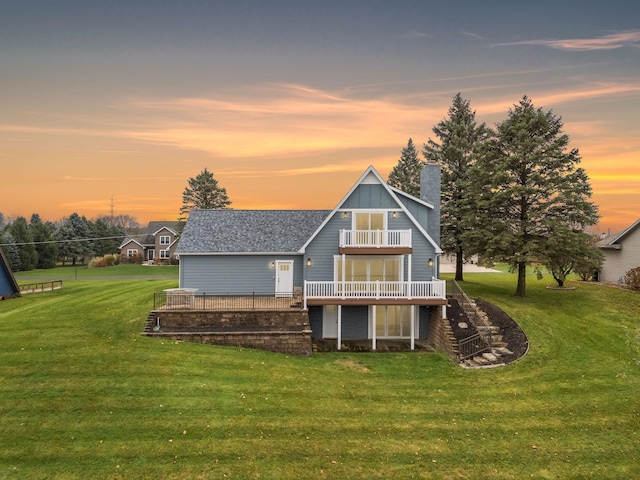 back house at dusk featuring a yard, a balcony, and a deck