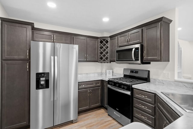 kitchen with dark brown cabinetry, sink, light wood-type flooring, and appliances with stainless steel finishes