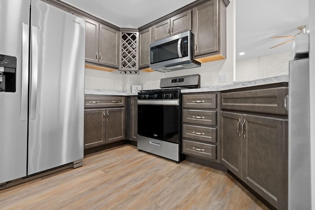 kitchen with light stone counters, dark brown cabinetry, stainless steel appliances, ceiling fan, and light hardwood / wood-style flooring