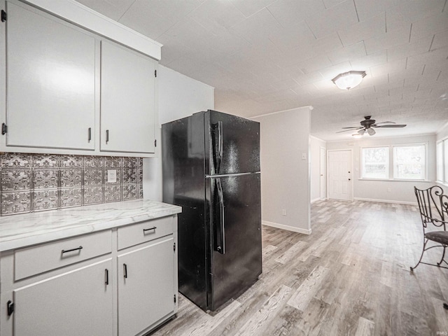 kitchen with white cabinets, black fridge, light hardwood / wood-style flooring, ceiling fan, and tasteful backsplash