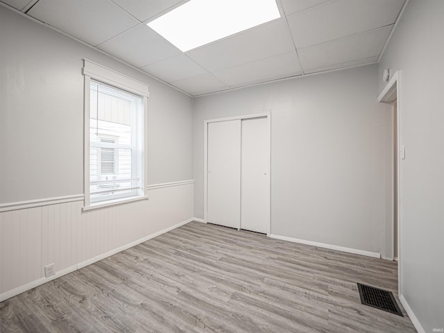 unfurnished bedroom featuring a paneled ceiling, a closet, and light wood-type flooring