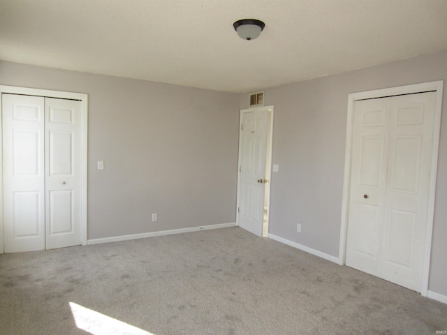 unfurnished bedroom with light colored carpet and two closets