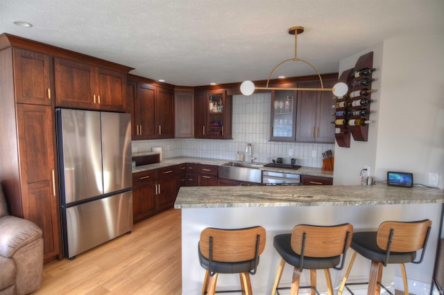 kitchen featuring sink, light hardwood / wood-style flooring, backsplash, kitchen peninsula, and appliances with stainless steel finishes