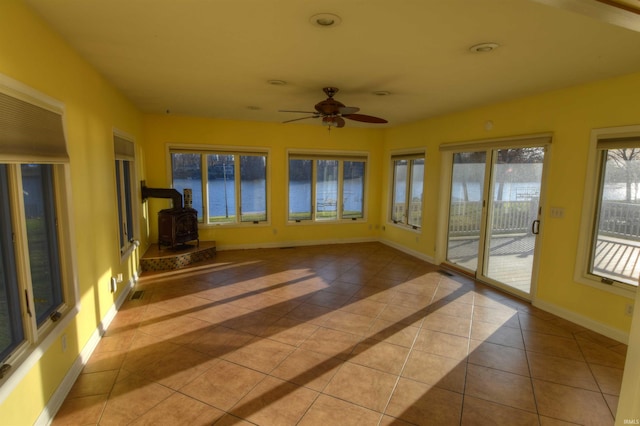 unfurnished sunroom featuring a wood stove, ceiling fan, and a water view