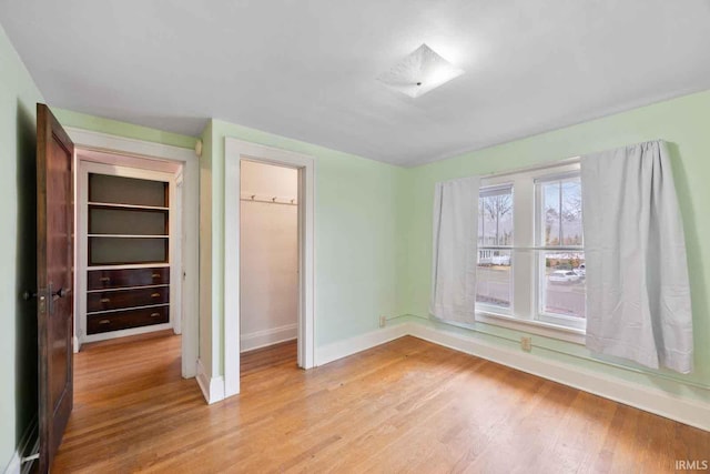 unfurnished bedroom featuring a spacious closet, a closet, and light wood-type flooring