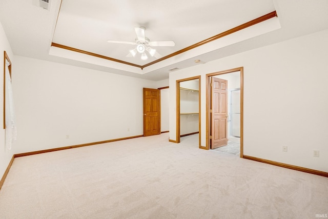 unfurnished bedroom with a raised ceiling, a walk in closet, ceiling fan, and light colored carpet