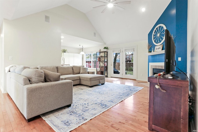 living room featuring ceiling fan, light wood-type flooring, a fireplace, and high vaulted ceiling