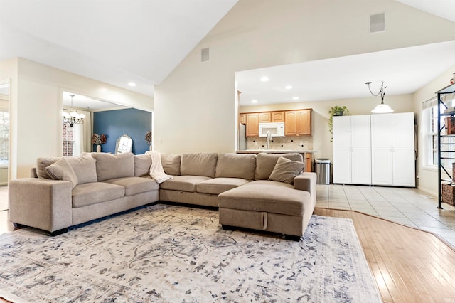 living room featuring sink, high vaulted ceiling, a notable chandelier, and light wood-type flooring