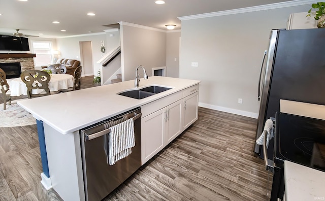 kitchen with stainless steel dishwasher, sink, white cabinets, a stone fireplace, and an island with sink