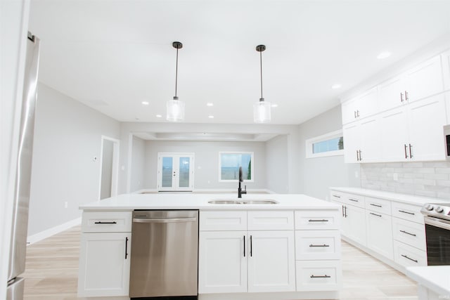 kitchen featuring white cabinetry, sink, stainless steel appliances, decorative light fixtures, and a kitchen island with sink