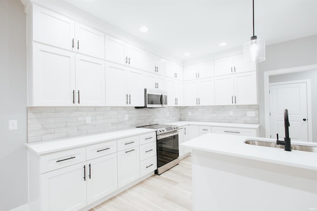 kitchen with pendant lighting, sink, light wood-type flooring, appliances with stainless steel finishes, and white cabinetry