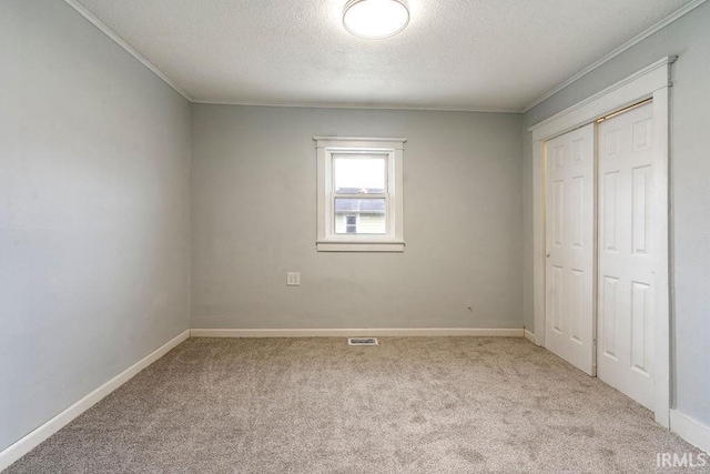 unfurnished bedroom with light carpet, a textured ceiling, a closet, and ornamental molding