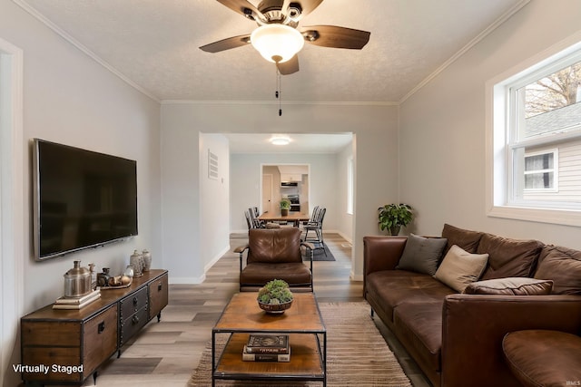 living room featuring ceiling fan, ornamental molding, a textured ceiling, and light wood-type flooring