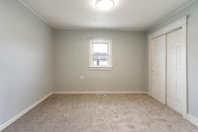 unfurnished bedroom with light carpet, a closet, a textured ceiling, and ornamental molding