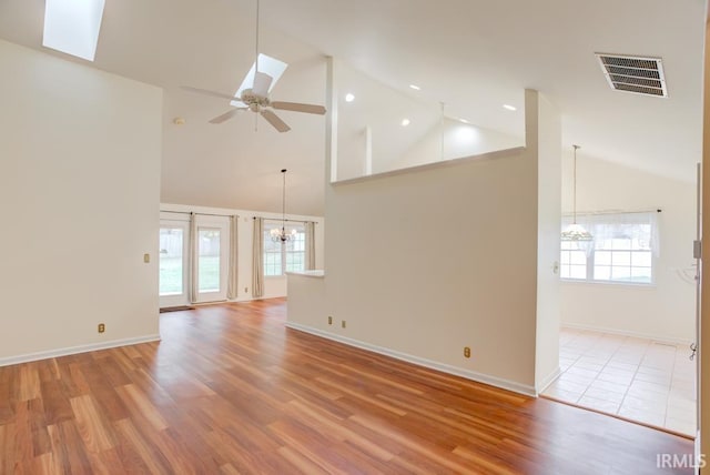 unfurnished living room with a wealth of natural light, light hardwood / wood-style floors, ceiling fan with notable chandelier, and high vaulted ceiling