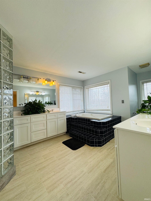 bathroom featuring tiled tub, vanity, a healthy amount of sunlight, and a textured ceiling