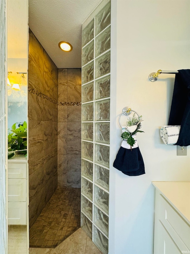 bathroom featuring tile patterned flooring, vanity, a textured ceiling, and tiled shower