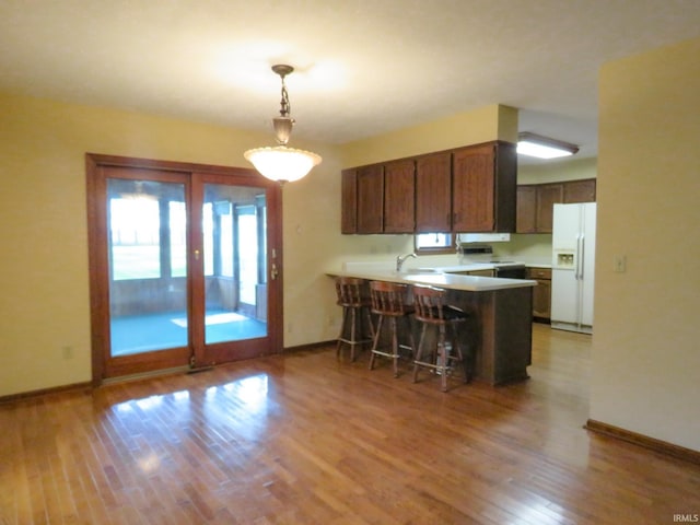 kitchen featuring kitchen peninsula, a breakfast bar, white appliances, decorative light fixtures, and light hardwood / wood-style floors