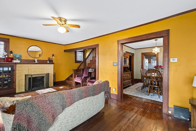 living room featuring a brick fireplace, crown molding, ceiling fan, and dark wood-type flooring