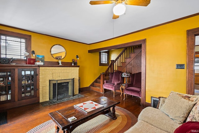 living room with ceiling fan, dark hardwood / wood-style flooring, crown molding, and a brick fireplace