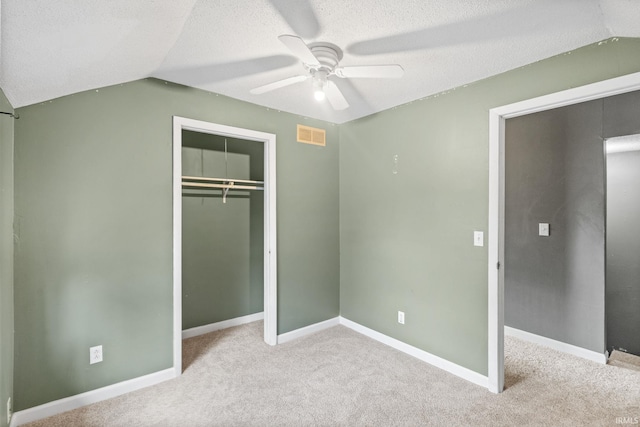 unfurnished bedroom featuring ceiling fan, light colored carpet, a textured ceiling, vaulted ceiling, and a closet