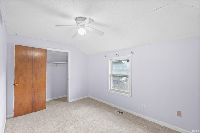 unfurnished bedroom with lofted ceiling, ceiling fan, a textured ceiling, light colored carpet, and a closet