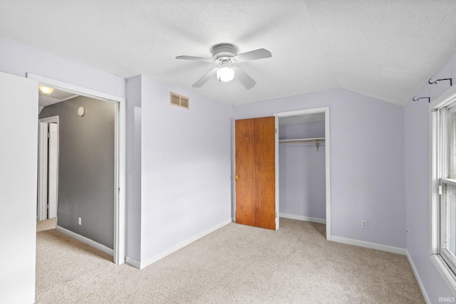 unfurnished bedroom featuring ceiling fan, a textured ceiling, vaulted ceiling, light carpet, and a closet