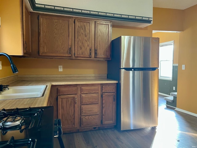 kitchen with stainless steel fridge, black gas stove, dark wood-type flooring, and sink