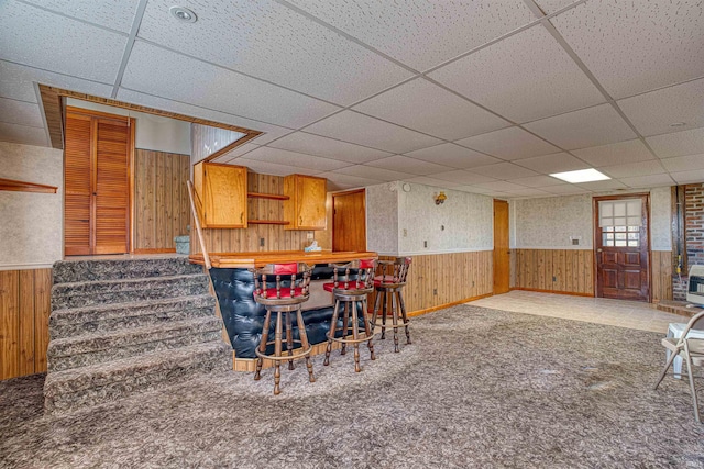 carpeted dining area featuring a paneled ceiling and wood walls