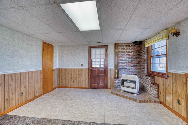 tiled living room featuring a paneled ceiling, wood walls, and heating unit