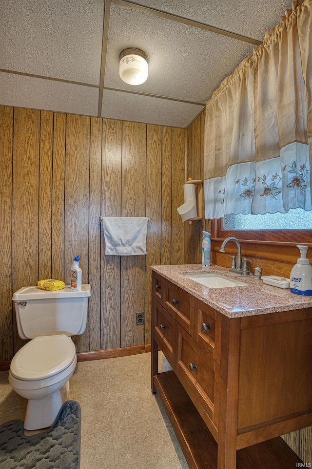 bathroom featuring vanity, toilet, a textured ceiling, and wooden walls