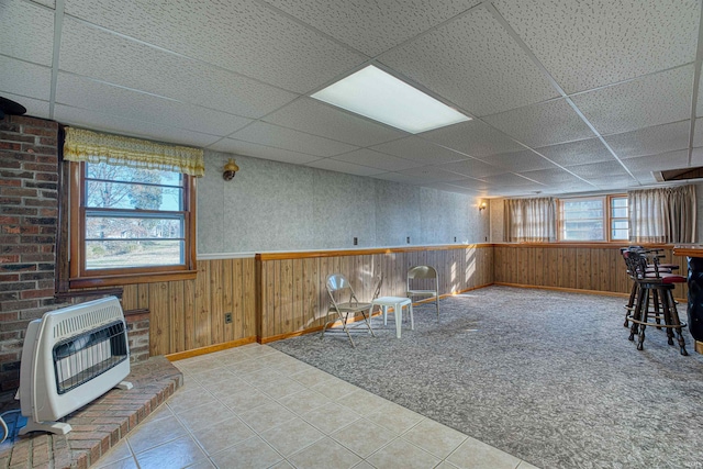 interior space with a paneled ceiling, wooden walls, and heating unit