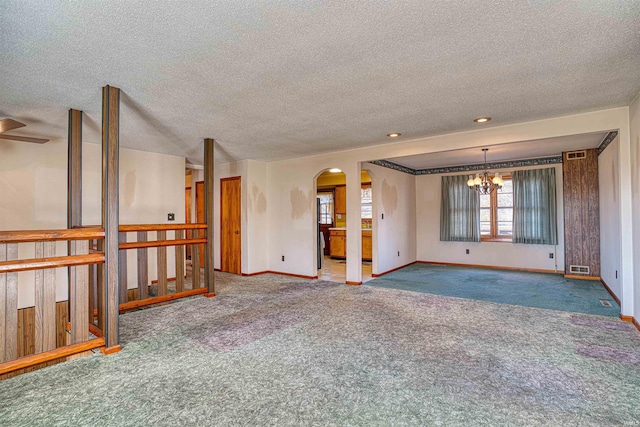 unfurnished room with carpet, a textured ceiling, and a notable chandelier