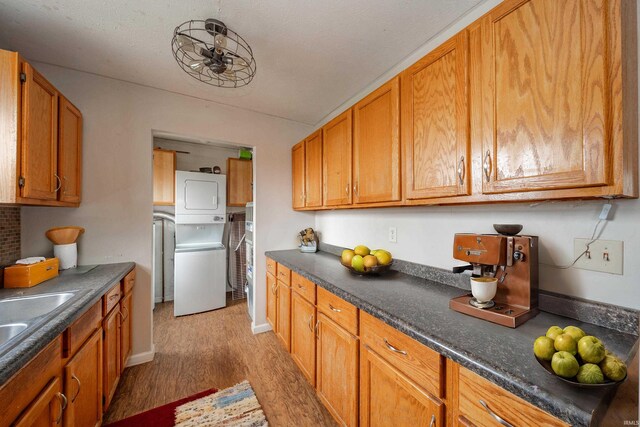 kitchen with a textured ceiling, sink, light hardwood / wood-style floors, and stacked washer / drying machine