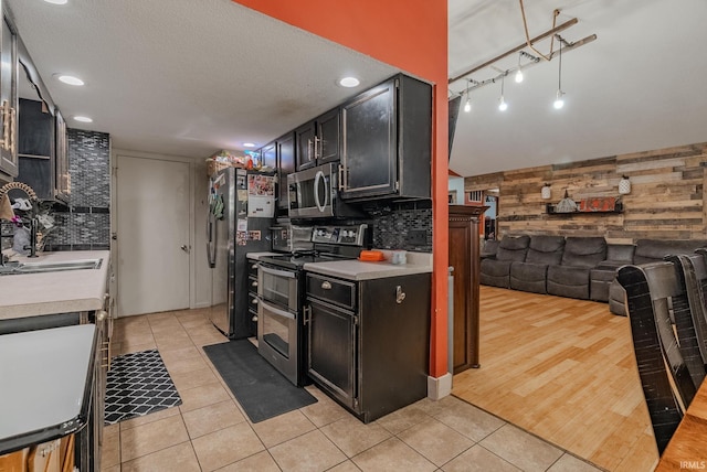 kitchen featuring sink, wooden walls, appliances with stainless steel finishes, tasteful backsplash, and light hardwood / wood-style floors