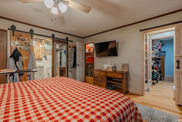 bedroom featuring ceiling fan, a barn door, crown molding, ensuite bathroom, and wood-type flooring