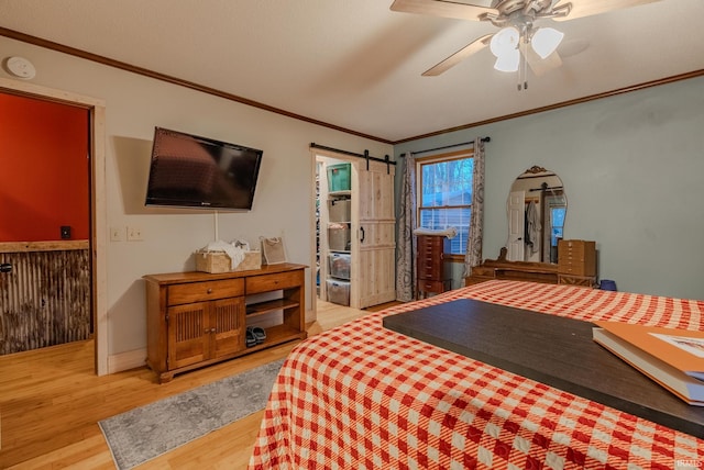 bedroom with hardwood / wood-style floors, ceiling fan, a barn door, and crown molding