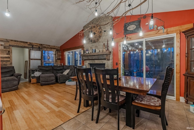 dining room featuring a stone fireplace, wood-type flooring, and lofted ceiling