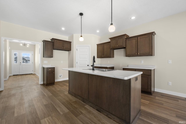 kitchen with pendant lighting, sink, dark brown cabinetry, an island with sink, and dark hardwood / wood-style flooring