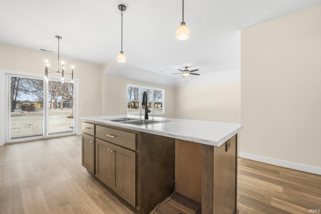 kitchen with an island with sink, pendant lighting, light hardwood / wood-style flooring, light stone counters, and sink