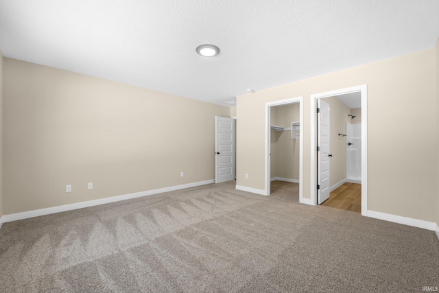 unfurnished bedroom with light colored carpet, a closet, a spacious closet, and connected bathroom