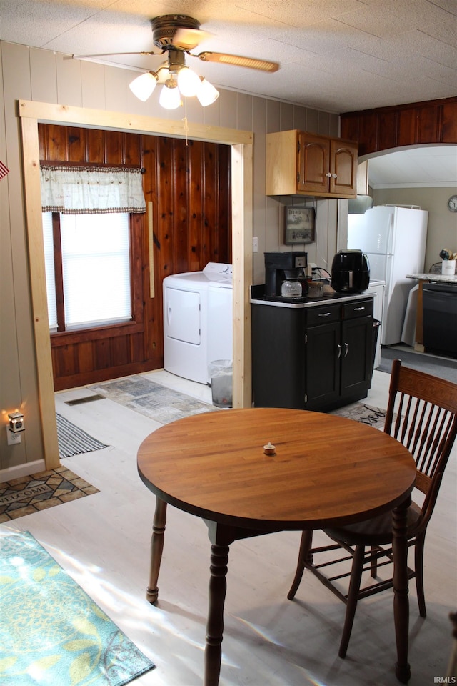 dining room featuring washer and dryer, a textured ceiling, ceiling fan, and wood walls