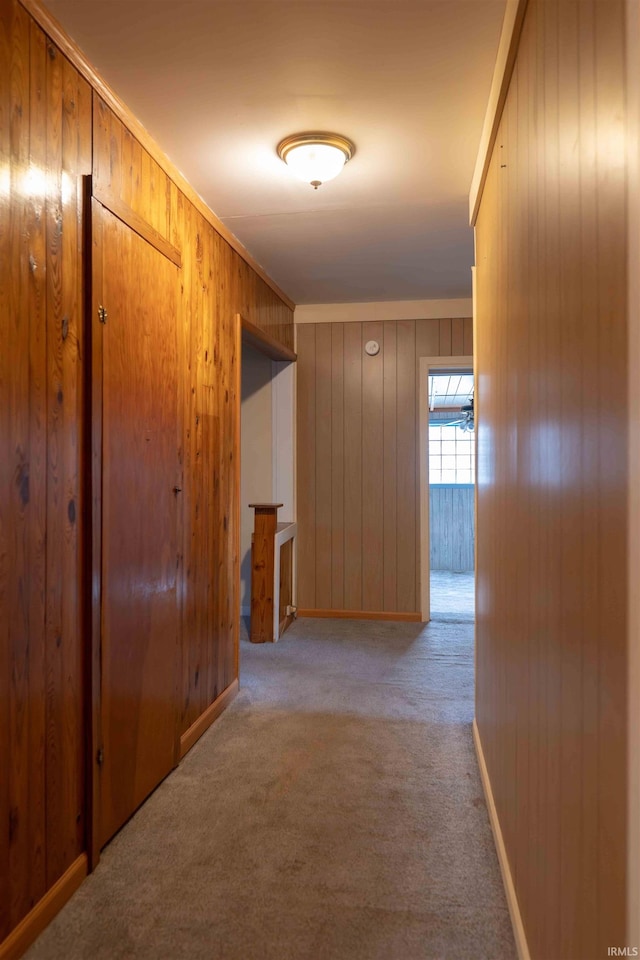 hall featuring light colored carpet, crown molding, and wooden walls