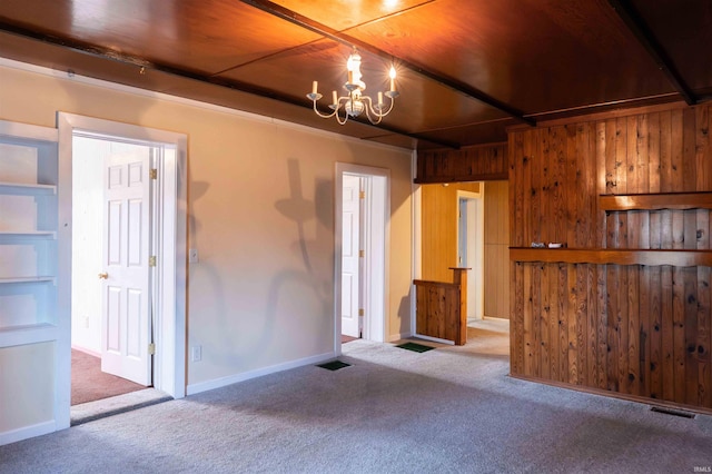 empty room with carpet, an inviting chandelier, and wood walls